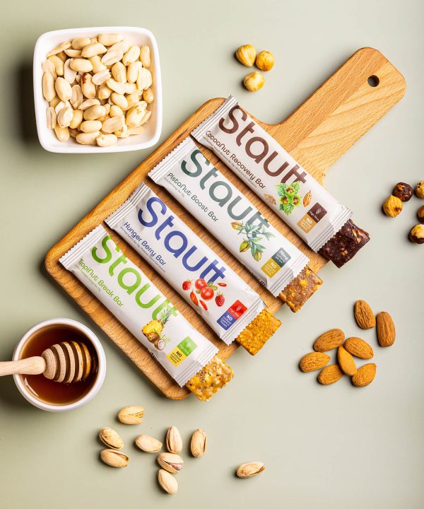 Barras nutricionais Stautt sobre tábua de madeira com frutos secos, vista de cima | Stautt nutrition bars on a wooden board with nuts, top view